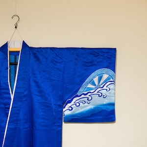 Puede incluir: Un kimono azul con un diseño de olas blancas y azules en la manga. El kimono está colgado en una percha.