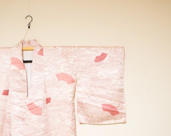 Könnte beinhalten: Ein rosafarbenes Seidenkimono mit einem traditionellen japanischen Fächermuster. Das Kimono hängt an einem Kleiderbügel.