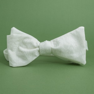 May include: A white bow tie with a textured pattern. The bow tie is made of a soft, silky fabric.