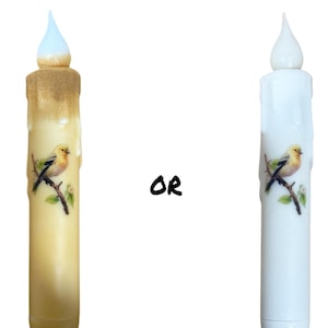 May include: Two battery-operated LED candles with a bird design. The candle on the left is yellow and the candle on the right is white.
