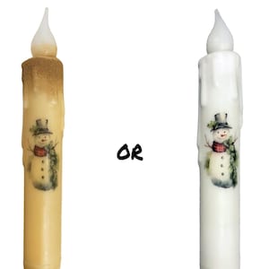 May include: Two white LED candles with a snowman design. The candle on the left is a warm yellow colour and the candle on the right is white. The text "OR" is printed in black between the candles.