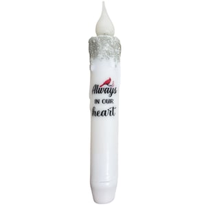 May include: White LED candle with a silver glitter finish and a red cardinal bird graphic. The candle has the text "Always in our heart" printed on it.