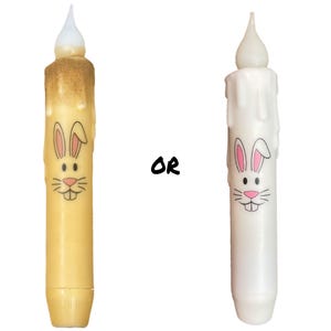 以下が含まれることがあります： 2つのイースターバニーキャンドルホルダー、1つは黄色、もう1つは白。どちらもピンクの耳と黒い鼻を持つウサギの顔をしています。