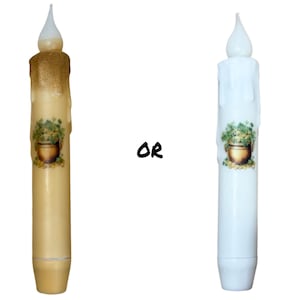 May include: Two LED candles with a dripping wax design. One candle is white and the other is a cream color. Both candles have a green shamrock design with a pot of gold.