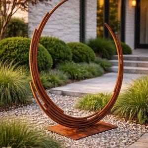 May include: A large, outdoor metal sculpture with a circular design. The sculpture is made of rusted metal and sits on a square base. The artwork is placed in a garden setting with greenery and small stones.