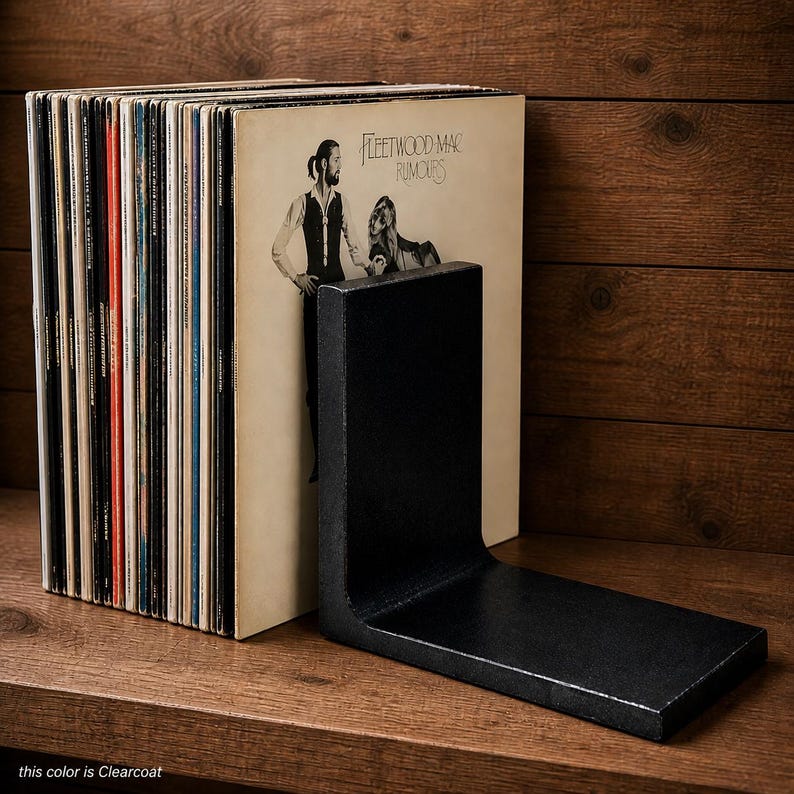May include: A black, L-shaped metal bookend supports a stack of vinyl records. The album cover of Fleetwood Mac's Rumours is visible. The text at the bottom of the image reads "this color is Clearcoat."