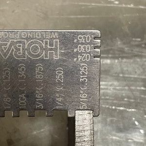 May include: A close-up of a stainless steel welding gauge with measurements in inches. The gauge has markings for 1/8", 3/16", 1/4", and 5/16". The text "HOBA WELDING PRO" is visible.