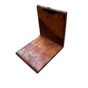 May include: A copper-colored, L-shaped metal bracket. The bracket has a weathered appearance with dark brown and light brown tones. The metal appears to have a slightly textured surface, with some areas showing signs of oxidation.
