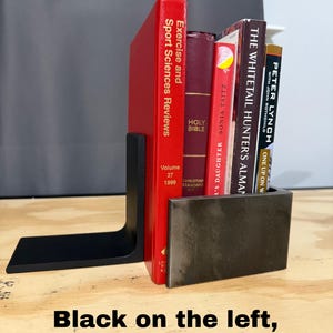 May include: A black metal bookend supports a collection of books with red, burgundy, and tan covers. The books include titles like "Exercise and Sport Sciences Reviews" and "Holy Bible." The text "Black on the left, clear on the right!" is at the bottom.