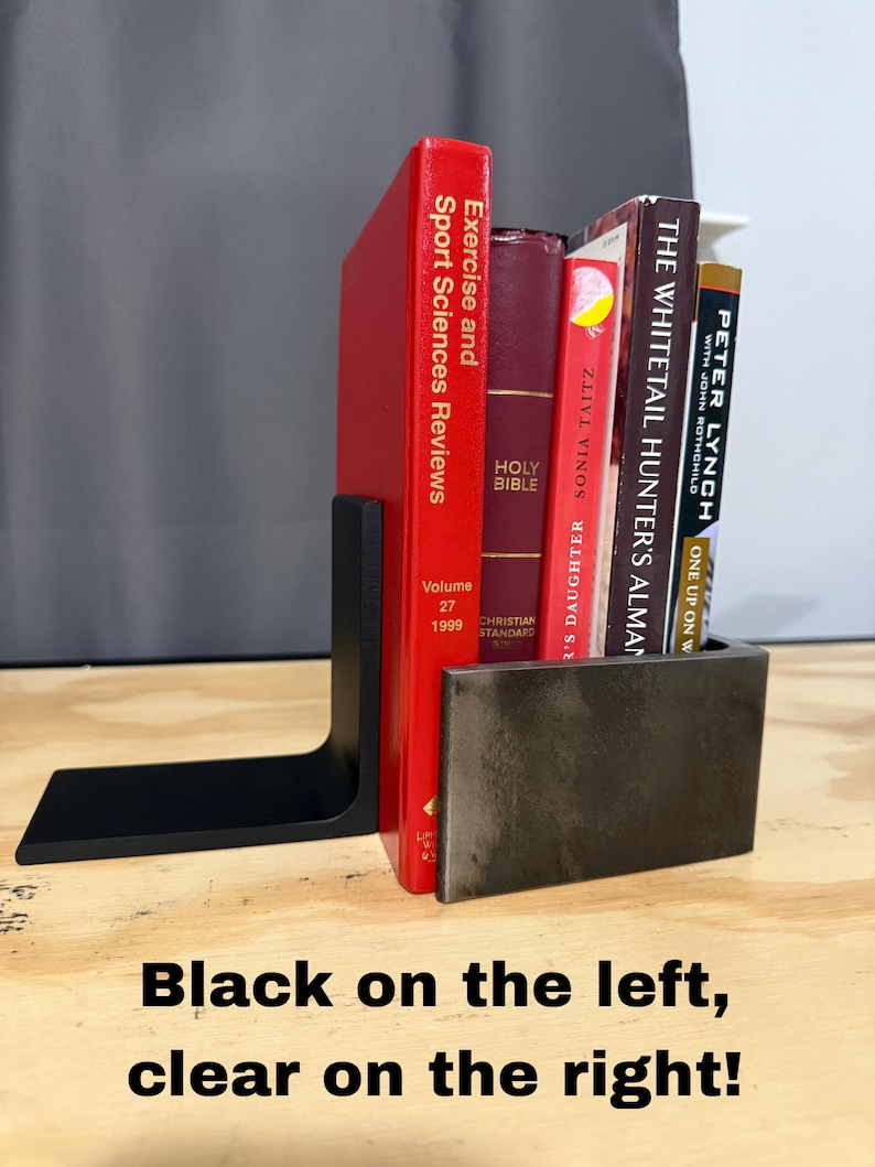 May include: A black metal bookend supports a collection of books with red, burgundy, and tan covers. The books include titles like "Exercise and Sport Sciences Reviews" and "Holy Bible." The text "Black on the left, clear on the right!" is at the bottom.