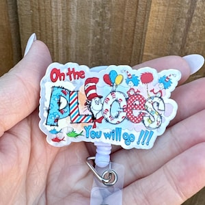 May include: A badge reel with a colorful design featuring text that reads "Oh the Places You will go !!!". The design includes illustrations of characters and elements from a children's book.