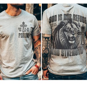May include: Light gray t-shirt with a cross and the text "46 1-3 PSALM" on the front. The back of the shirt features a lion graphic with the words "GOD IS OUR REFUGE AND STRENGTH" and "PSALM 46:1-3".