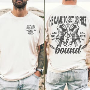 May include: A white t-shirt with a black graphic design of two hands breaking free from chains. The text "He came to set us free" and "I am no longer bound" is printed on the shirt. The back of the shirt has a quote from the Bible, John 8:36, "So if the Son sets you free, you will be freed indeed."