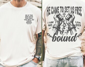 Op de afbeelding: Een wit T-shirt met een zwart grafisch ontwerp van twee handen die zich bevrijden van kettingen. De tekst "He came to set us free" en "I am no longer bound" staat op het T-shirt gedrukt. De achterkant van het T-shirt heeft een citaat uit de Bijbel, Johannes 8:36, "So if the Son sets you free, you will be freed indeed."