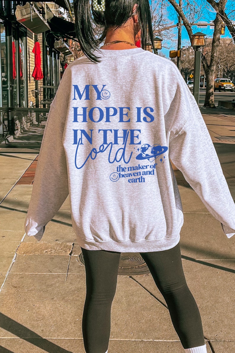 May include: A pale grey sweatshirt featuring the blue text "MY HOPE IS IN THE Lord". The design includes a smiley face, a planet, and the words "the maker of heaven and earth". The sweatshirt is a relaxed fit.