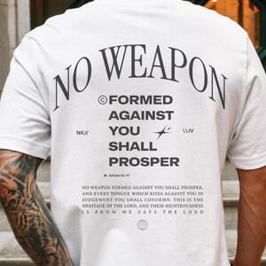 May include: White t-shirt with the text "NO WEAPON FORMED AGAINST YOU SHALL PROSPER" and the Bible verse "ISAIAH 54:17". The text is in black and the background is white.