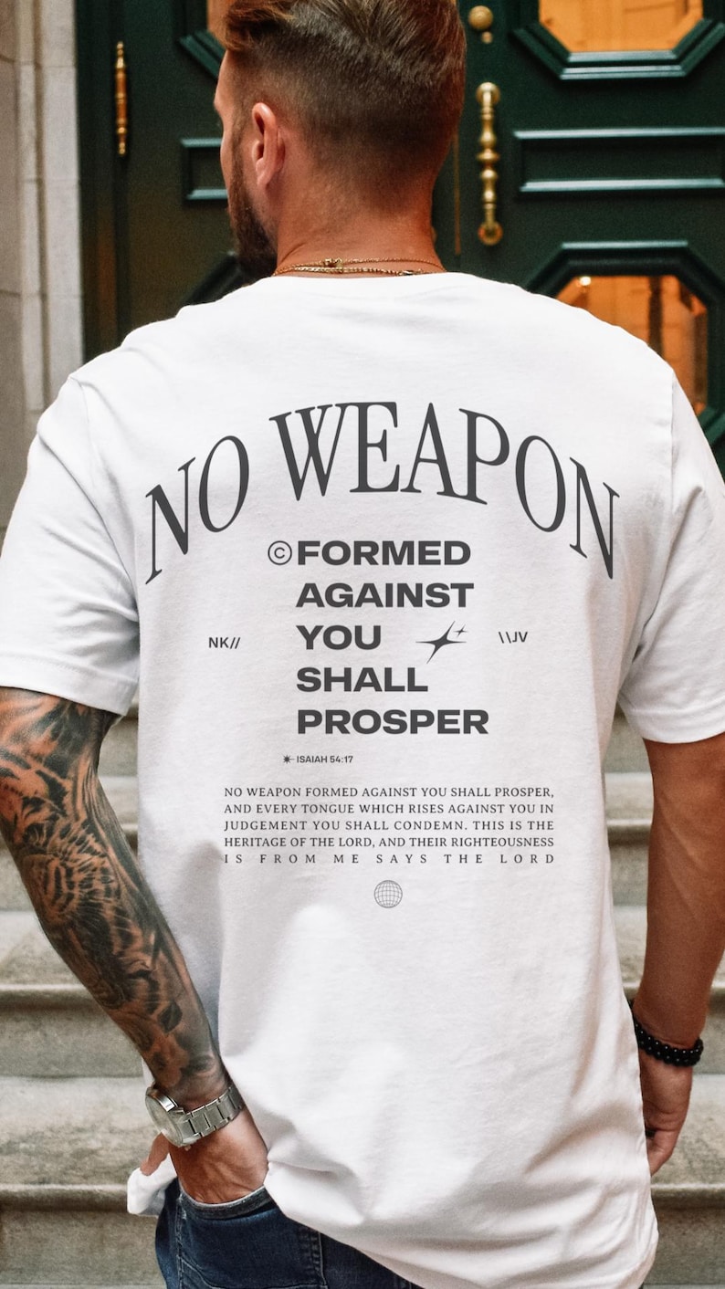 May include: White t-shirt with the text "NO WEAPON FORMED AGAINST YOU SHALL PROSPER" and the Bible verse "ISAIAH 54:17". The text is in black and the background is white.