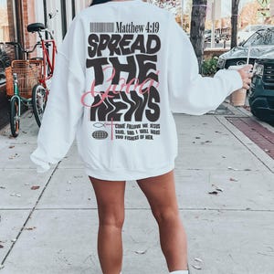 May include: White sweatshirt with a black and pink graphic print that says "Spread the Good News" and includes a bible verse, Matthew 4:19. The graphic also includes a fish and a globe.