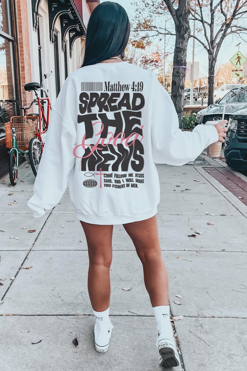 May include: White sweatshirt with a black and pink graphic print that says "Spread the Good News" and includes a bible verse, Matthew 4:19. The graphic also includes a fish and a globe.