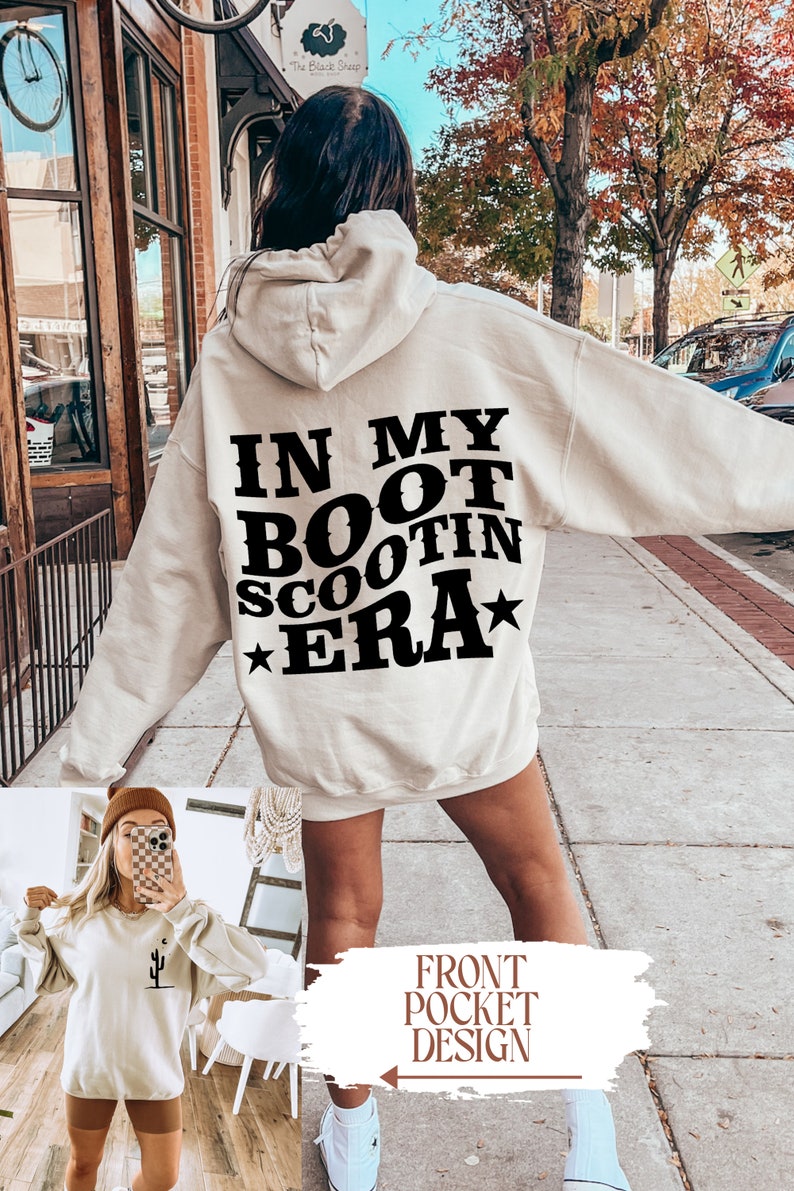 May include: A cream-colored hoodie with a black graphic that says "In My Boot Scootin Era" with a star on either side of the text. The hoodie has a front pocket and a drawstring hood. The model is wearing the hoodie with a pair of white sneakers.