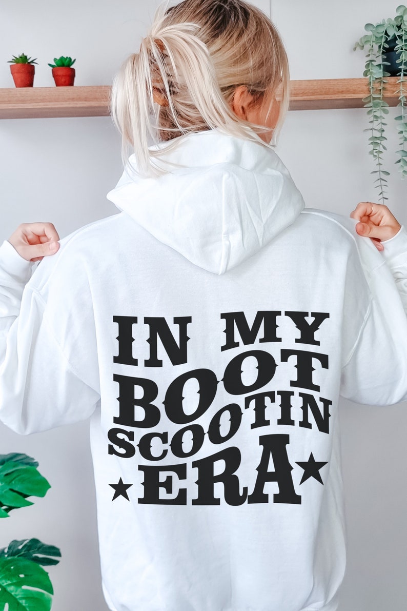 May include: White hoodie with black text that reads "In My Boot Scootin Era" with a star on either side of the text.