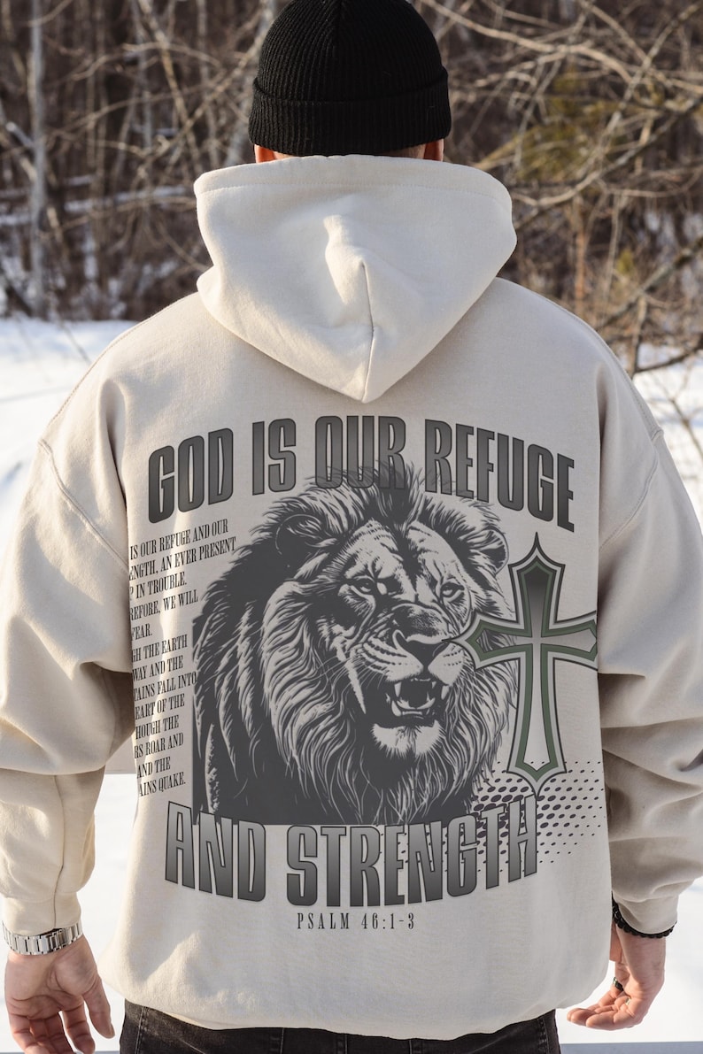 May include: Beige hoodie with the text "GOD IS OUR REFUGE AND STRENGTH" and a lion graphic. The back of the hoodie also features a cross and the Bible verse Psalm 46:1-3. The hoodie has a drawstring hood and long sleeves.