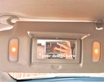 May include: A beige car sun visor with a mirror and two small lights. The mirror is open and shows a reflection of a person holding a mobile phone. The text "your design here" is written on the mirror.
