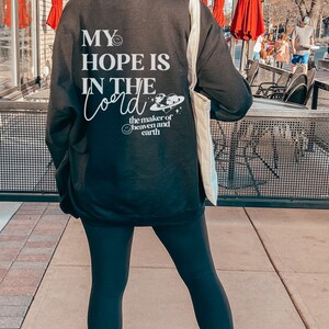 May include: Black sweatshirt with white text reading "MY HOPE IS IN THE Lord" and a graphic of the earth, with the words "the maker of heaven and earth." The sweatshirt is worn with black leggings and white trainers.