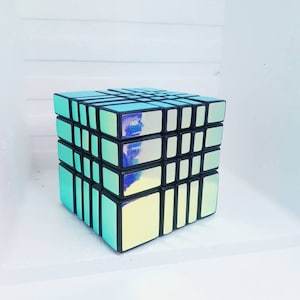 Puede incluir: Un rompecabezas de cubo 5x5 azul iridiscente y negro. El cubo está hecho de plástico y tiene una superficie reflectante.