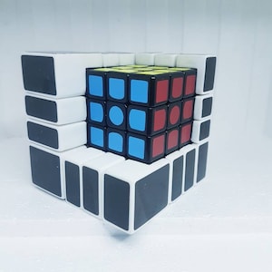 May include: A black and white Rubik's cube with red, blue and yellow squares on the visible faces. The cube is partially disassembled, with some of the outer pieces removed.