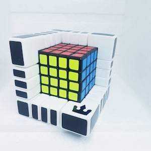 May include: A complex puzzle cube featuring a 4x4x4 Rubik's Cube at its centre. The outer structure is white with black detailing and a crown logo. The central cube has red, yellow, blue, and green squares.