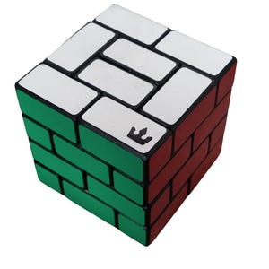 Puede incluir: Un cubo de rompecabezas con un patrón de ladrillos en sus caras. La superficie superior es blanca, el lado frontal izquierdo es verde y el lado frontal derecho es rojo. Un logotipo negro en forma de corona está impreso en una de las piezas blancas.
