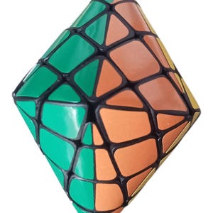 May include: A diamond-shaped puzzle cube featuring a black plastic frame with irregular, multi-sided segments. The surface is divided into vibrant green and orange panels, creating a complex geometric pattern across the entire structure.