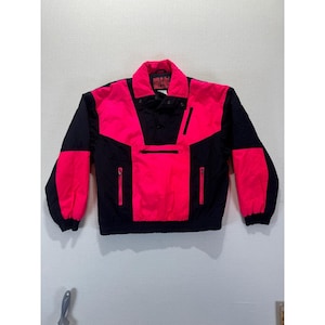 May include: A black and hot pink vintage anorak jacket. The jacket has a high collar, a front pocket, and two side pockets. The sleeves and shoulders are black, while the chest and upper back are hot pink. The jacket has a drawstring at the waist.