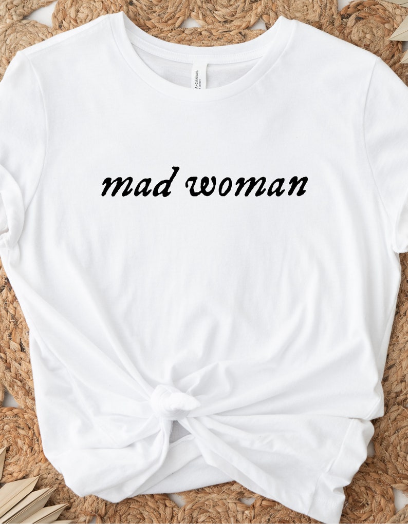 May include: White t-shirt with the text "mad woman" in black cursive lettering.