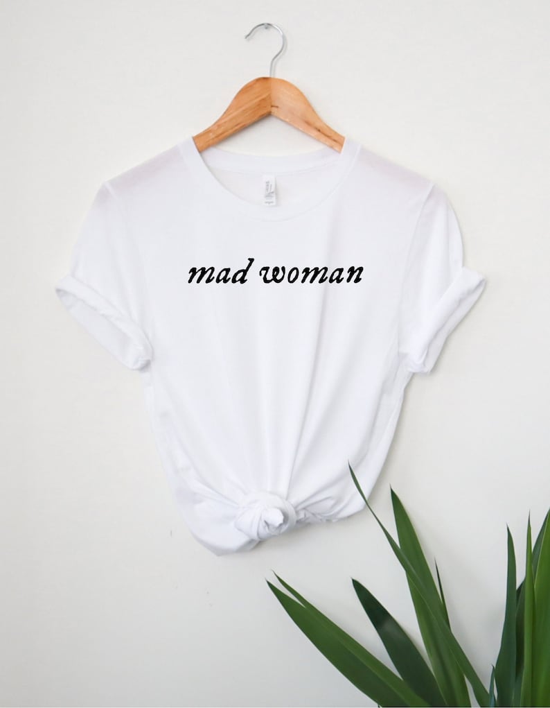 May include: White t-shirt with the text "mad woman" in black cursive lettering.