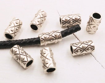 May include: Silver metal beads with a geometric pattern, designed for use with leather cord. The beads have a slightly rounded shape and a smooth, polished finish.