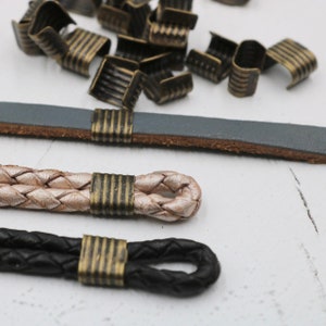 May include: Three leather cords with brass end caps. The cords are braided and come in black, beige, and gray. The brass end caps have a ridged design.