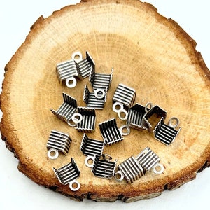 May include: Silver metal clasps with a ridged design. The clasps have a small loop on the top for attaching to a cord or chain.