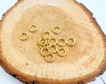May include: A pile of gold jump rings on a wooden surface. The rings are small and round, and they are perfect for jewelry making.
