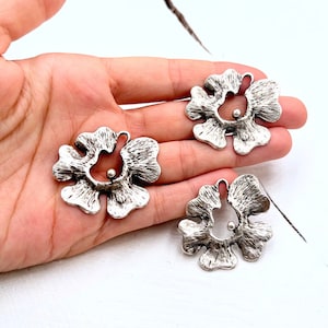 May include: Two silver metal flower-shaped charms with a small bead in the center of each. The charms have a textured surface and a slightly irregular shape.
