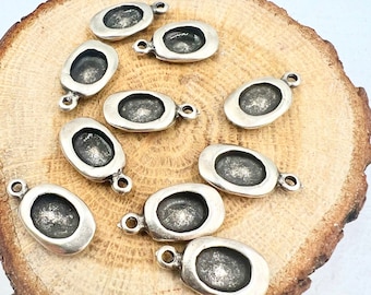 May include: Ten silver oval-shaped charms with a loop at the top. The charms are arranged on a wooden surface.