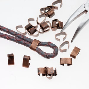 May include: A close-up of a leather cord with a copper clasp and a pile of copper jump rings. A pair of pliers is also visible in the image.