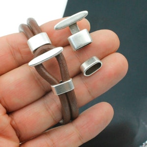 May include: A brown leather bracelet with silver metal clasps and end caps. The bracelet is double-layered and has a simple design.