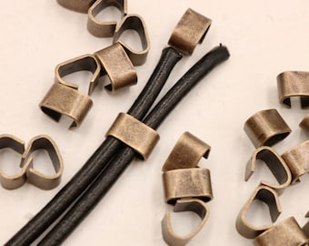 May include: A close-up of antique gold metal cord ends for leather cord. The cord ends are designed to hold two cords together. There are multiple cord ends scattered around the image.
