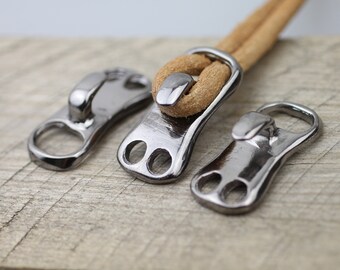 May include: Three silver metal zipper pulls with a loop on one end and two holes on the other. One pull has a brown leather cord threaded through it.