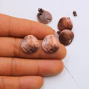 May include: A set of six copper-toned metal earring blanks. The blanks are round and have a hammered texture. Each blank has a small hole in the center for attaching earring findings.
