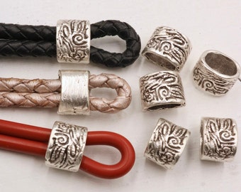 May include: Silver metal beads with a decorative design. The beads are shown on different colored leather cords.