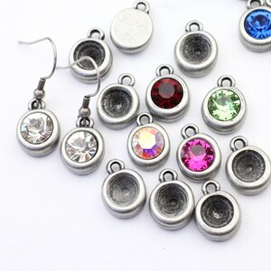 May include: Assortment of silver-toned earring settings with various colored rhinestones. The settings are round and have a small loop at the top for attaching to earrings. The rhinestones are red, green, blue, pink, and clear.