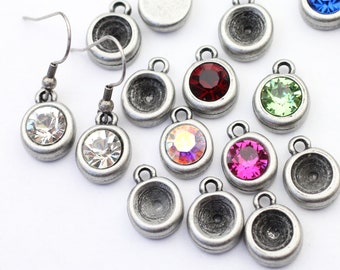 May include: Assortment of silver-toned earring settings with various colored rhinestones. The settings are round and have a small loop at the top for attaching to earrings. The rhinestones are red, green, blue, pink, and clear.